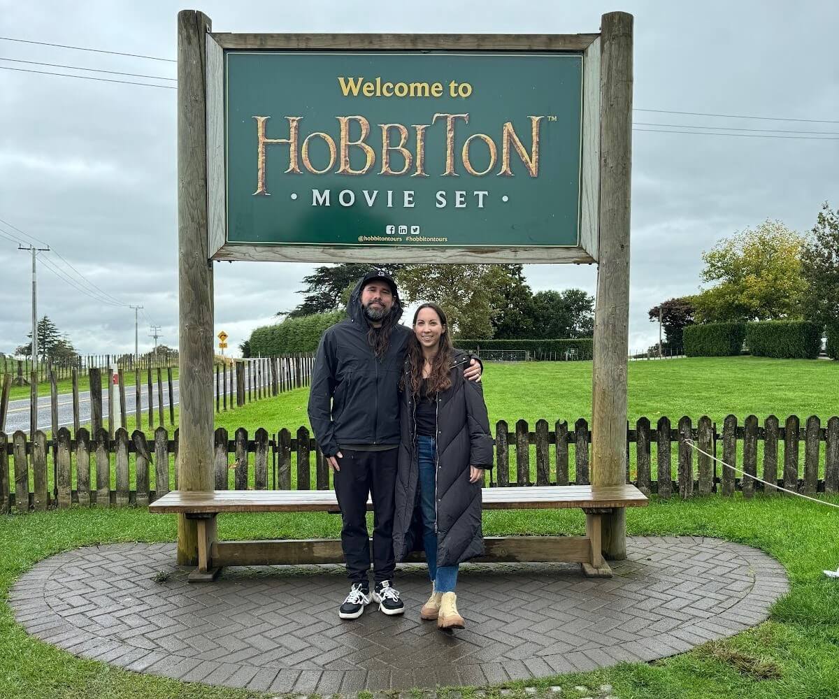 A man and a woman standing in front of a big Hobbiton Movie sign
