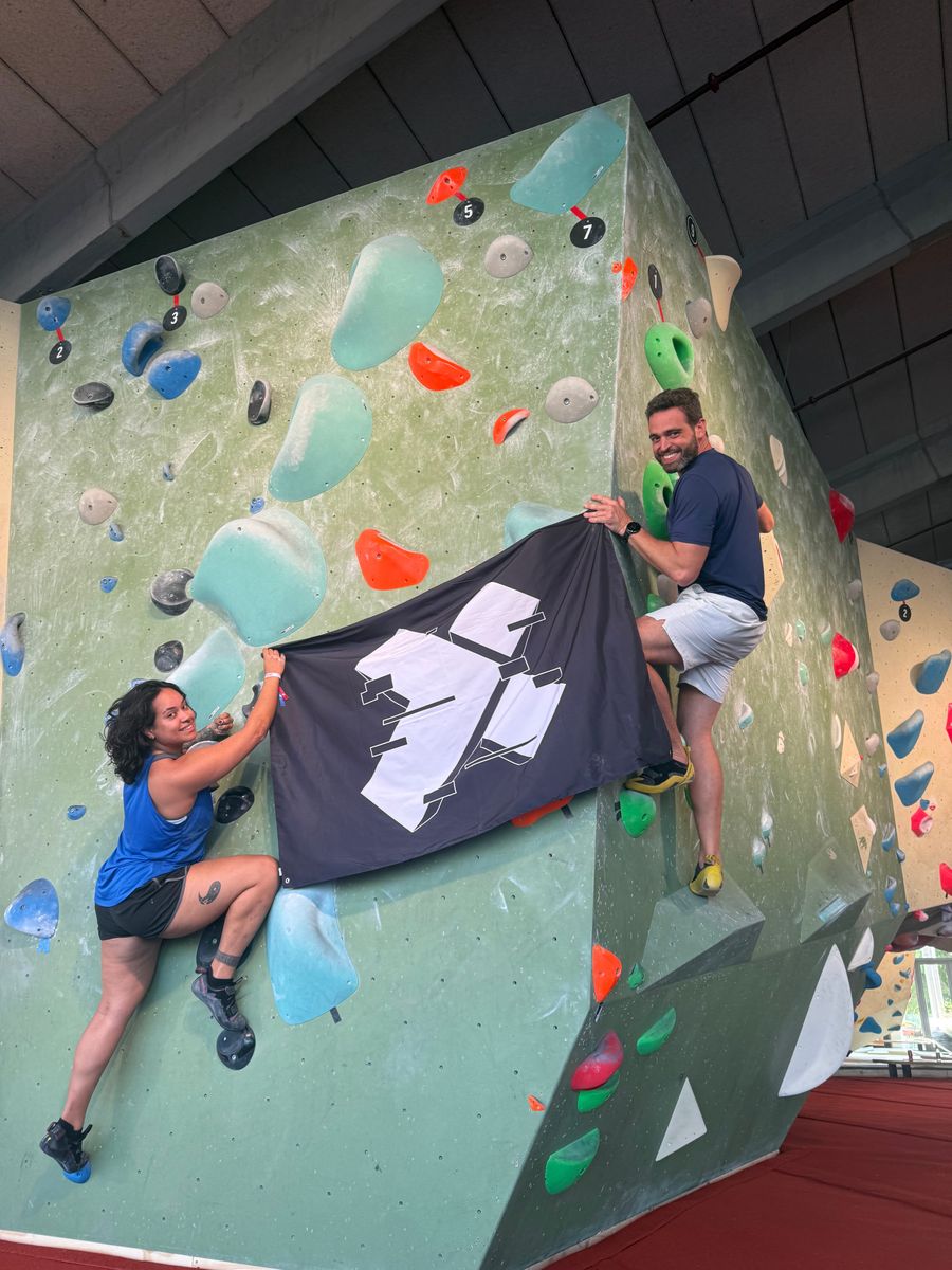 An X-Teamer climbing a bouldering wall with the X-Team flag at an X-Outpost