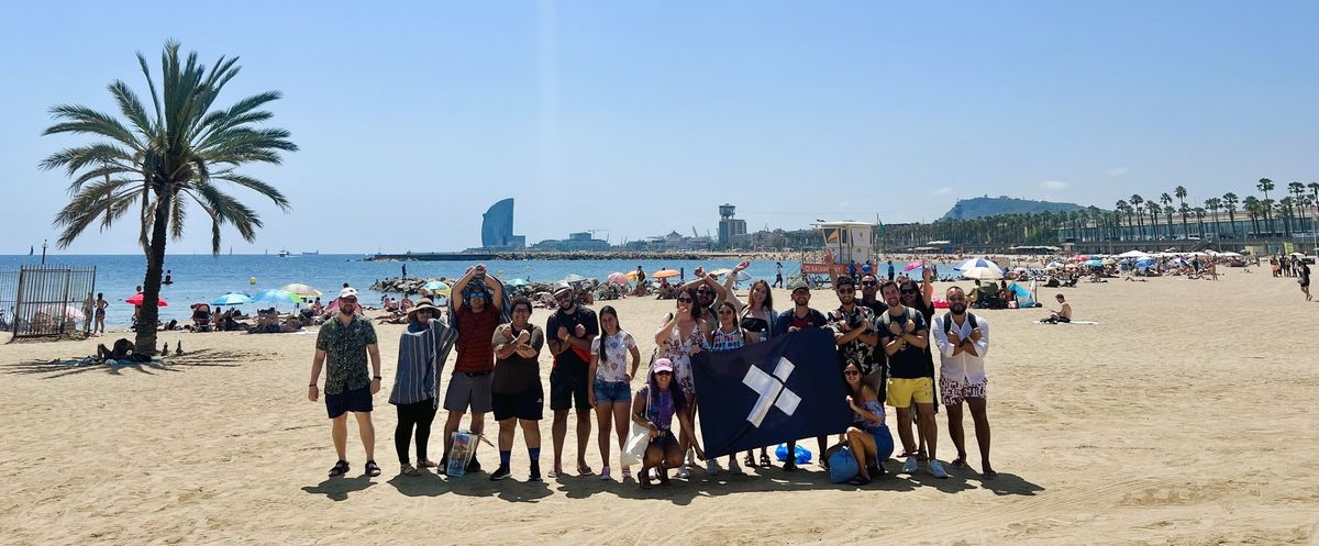 A large group of X-Teamers on the beach in Barcelona with the X-Team flag
