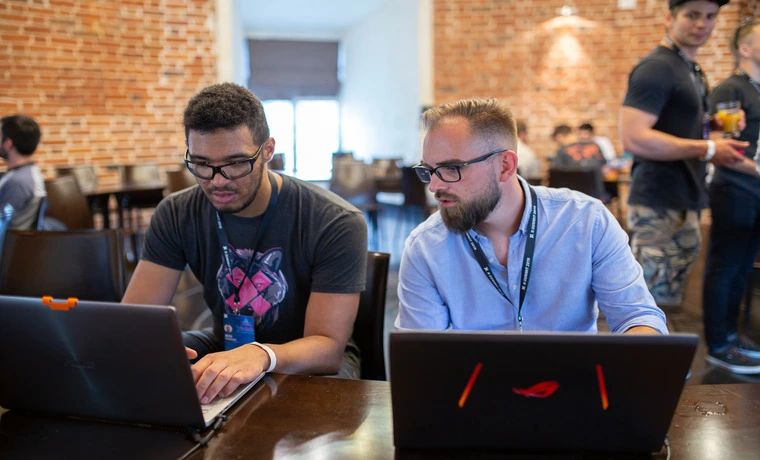 Two X-Team developers pairing on laptops at a coworking meetup